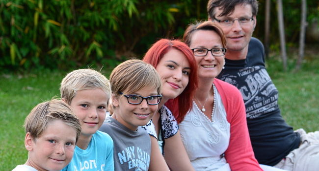 Foto: Eine sechsköpfige Familie sitzt auf einer Wiese und schaut in die Kamera